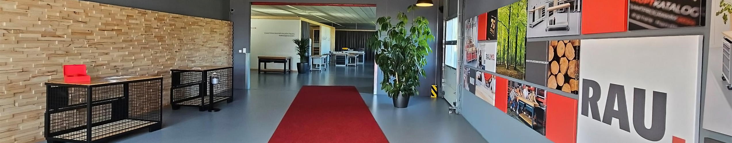 Korridor mit Holzwänden, rotem Teppich, Pflanzen und Bildern an den Wänden. Tische stehen im Hintergrund.